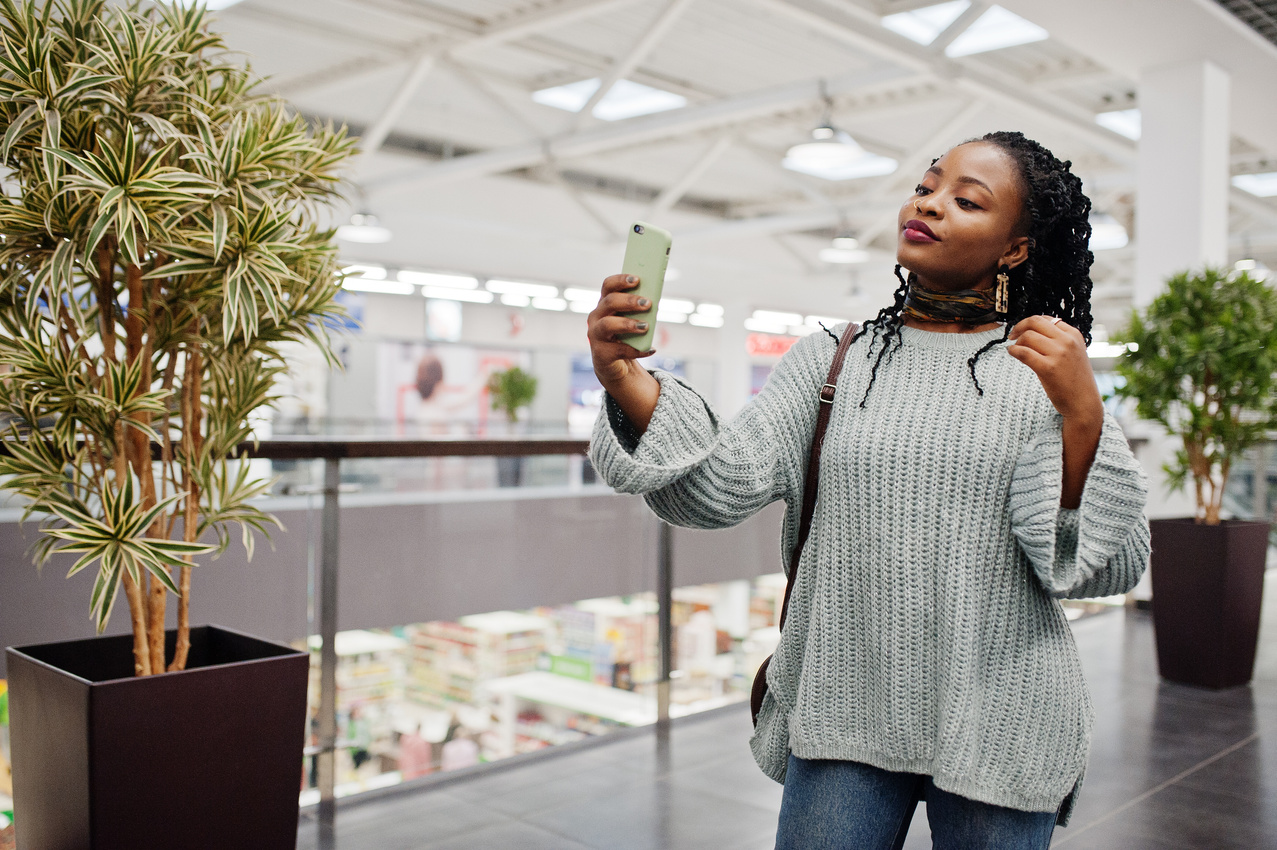 African woman bloger posed in sweater and jeans posed at mall wi